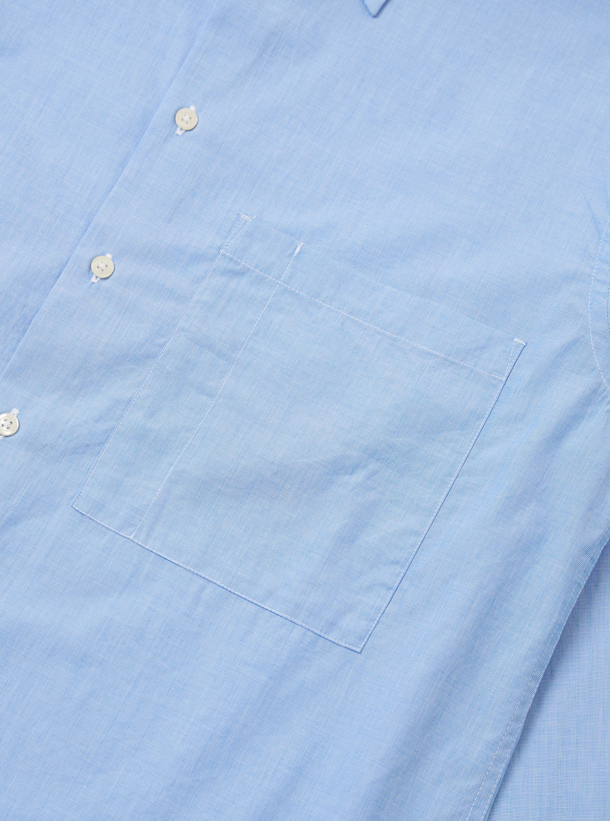 The Sky Fil A Fil Square Pocket Shirt is shown as a flat lay against a white background. The shirt features a large, oversized square chest pocket on the left side, a button-front fastening, and a pointed collar. The fabric is a light sky blue with a visible fil-a-fil weave.