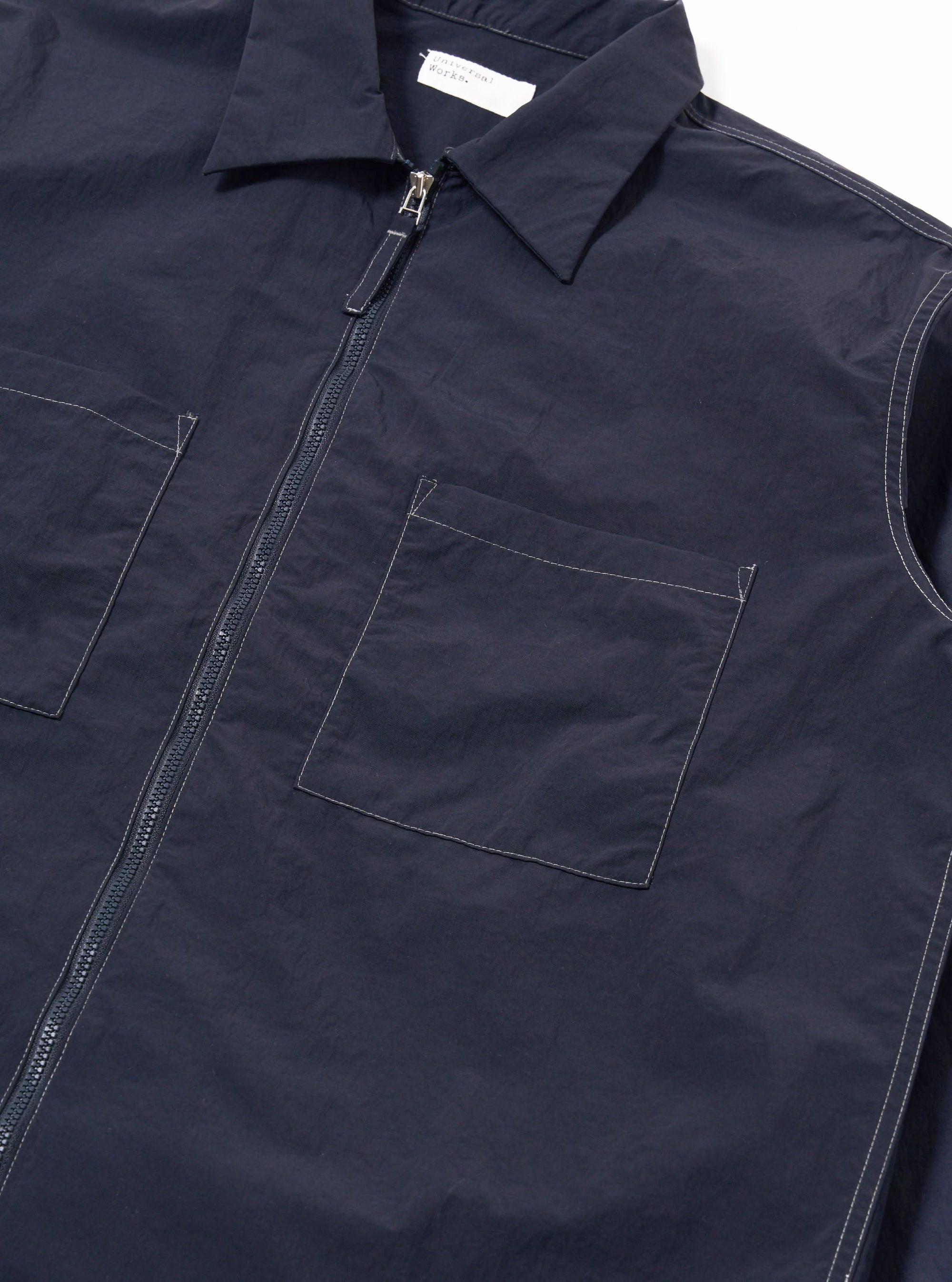 The Navy Seo Recycled Nylon Zip Too Shirt is shown in a detail view as a flat lay against a plain white background. The image highlights the smooth, technical finish of the navy blue recycled nylon fabric and the clean stitching around the zip-front closure.
