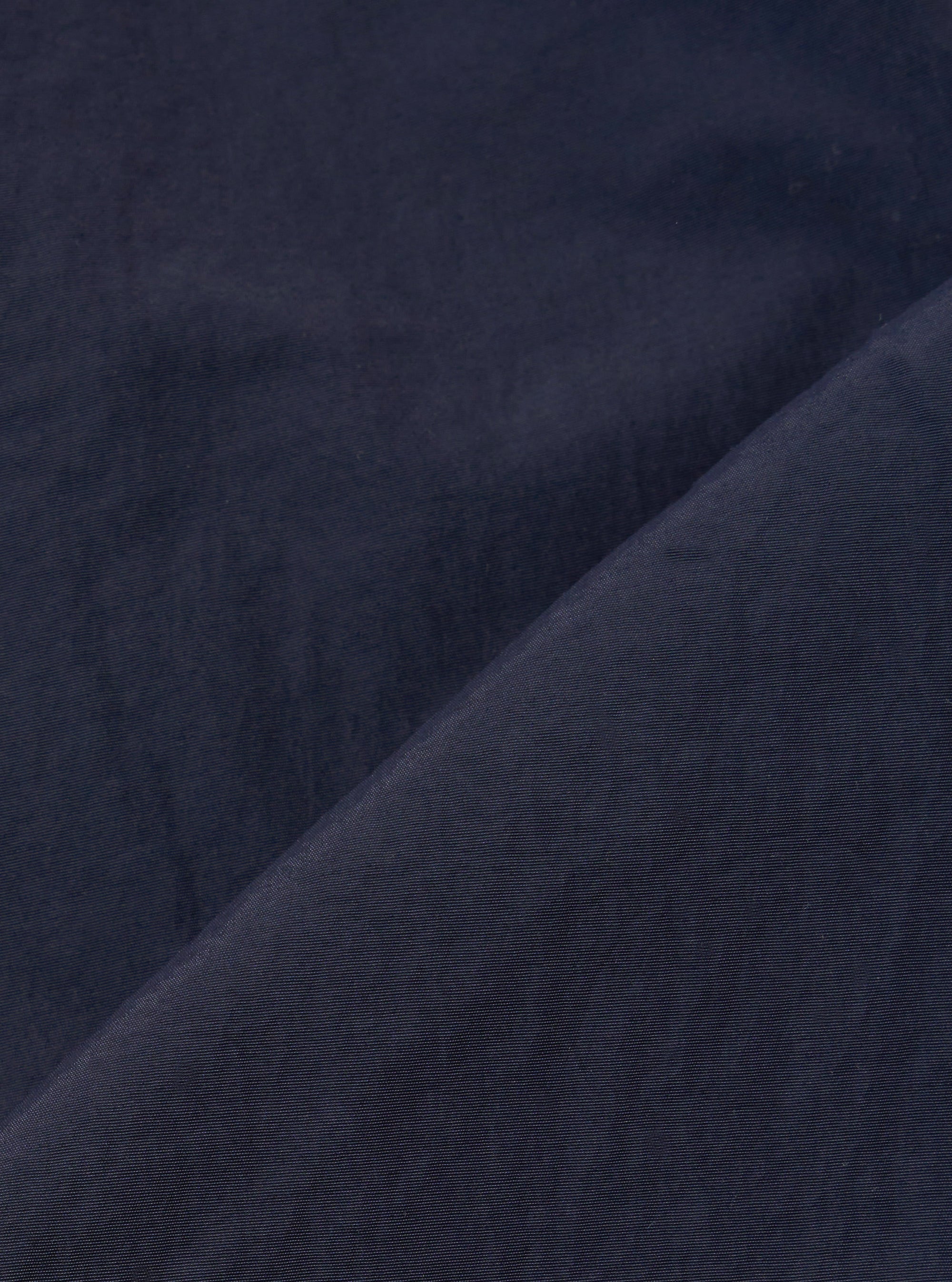 A close-up fabric swatch of the Navy Seo Recycled Nylon Zip Too Shirt highlights the smooth, technical texture of the recycled nylon material. The fabric is a solid, deep navy blue with a slight matte finish and a visible fine-grained weave.