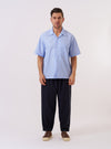 The Sky Fil A Fil Camp Shirt is shown as a flat lay against a plain white background. The shirt features a camp collar, a central button-down front with tonal buttons, and a single square patch pocket on the left chest. The light blue cotton fabric has a fine fil-a-fil weave, creating a subtle textured appearance.