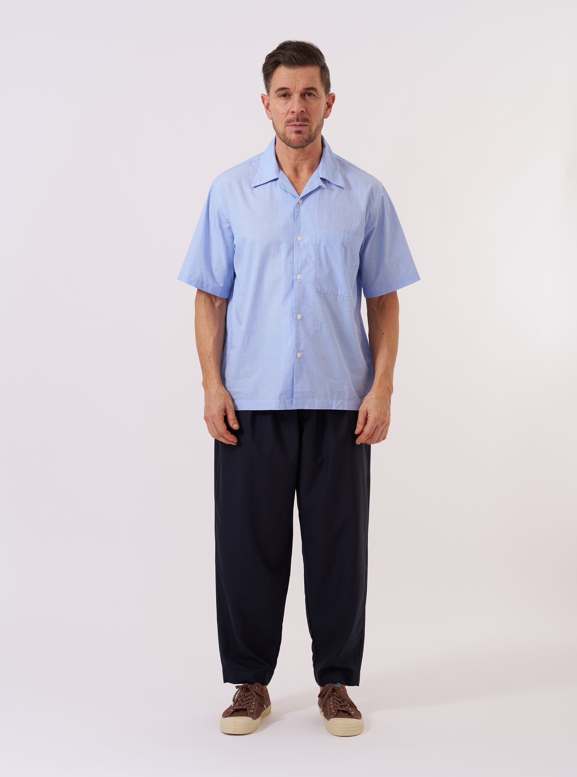 The Sky Fil A Fil Camp Shirt is shown as a flat lay against a plain white background. The shirt features a camp collar, a central button-down front with tonal buttons, and a single square patch pocket on the left chest. The light blue cotton fabric has a fine fil-a-fil weave, creating a subtle textured appearance.