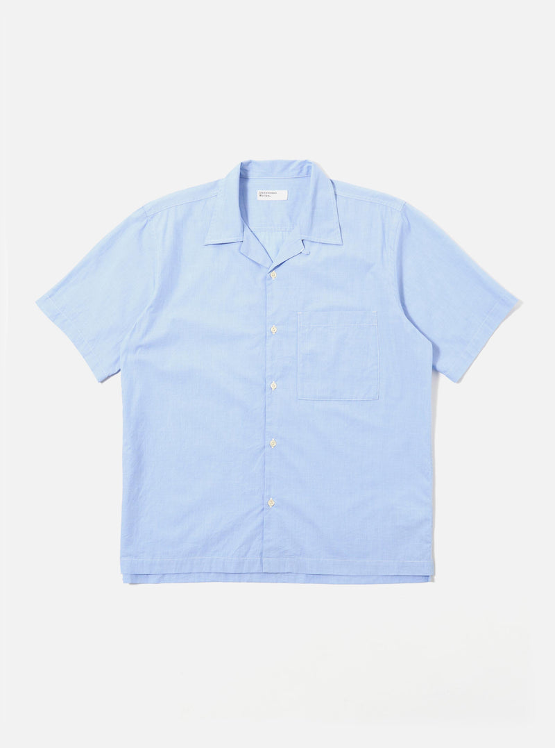 The Sky Fil A Fil Camp Shirt is shown as a flat lay against a white background. The short-sleeve shirt features a relaxed camp collar, a central six-button closure, and a single patch pocket on the left chest. The light blue cotton fabric has a fine, multi-tonal fil-a-fil weave.