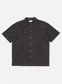 The Black Tech Cotton S/S Dwight Overshirt is shown as a flat lay against a white background. The short-sleeved overshirt features a straight hem, a button-down front with a camp collar, and four front patch pockets. Two rows of vertical sewn pleats run down the front on either side of the buttons. The fabric is a smooth black tech cotton.