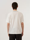 A model wears the Ecru Single Jersey 34 Printed Core Tee, shown from the back against a plain white background. The t-shirt features a relaxed, generous fit with a classic crew neckline and short sleeves. The ecru-colored cotton fabric is showcased alongside a small, woven branded label positioned near the hem on the lower left side.