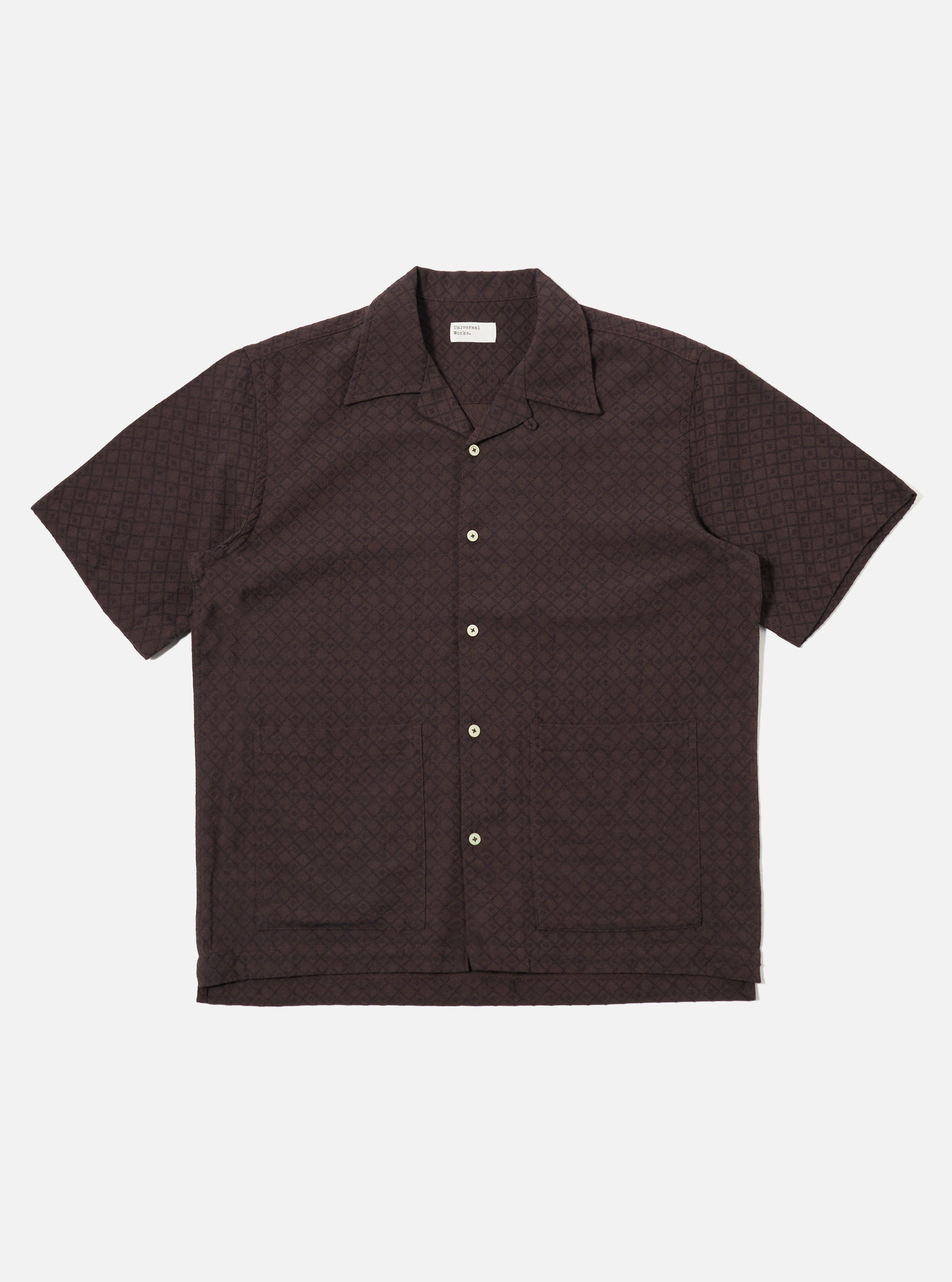 The Brown Diamond Dobby Deck Shirt is shown as a flat lay against a plain white background. The shirt features a one-piece collar, a central button-down front, and two large patch pockets at the waist. The brown cotton fabric has a distinct diamond dobby texture and the garment is designed with short, loose sleeves and a straight hem.