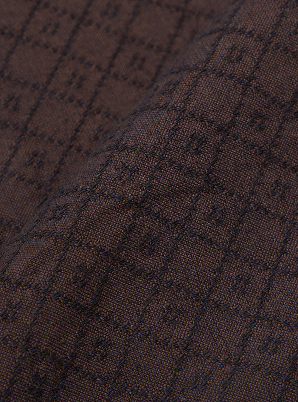 A close-up fabric swatch of the Brown Diamond Dobby Lucky Shirt displays a detailed view of the brown cotton material. The image highlights the intricate, geometric diamond dobby weave and the textured surface of the fabric.