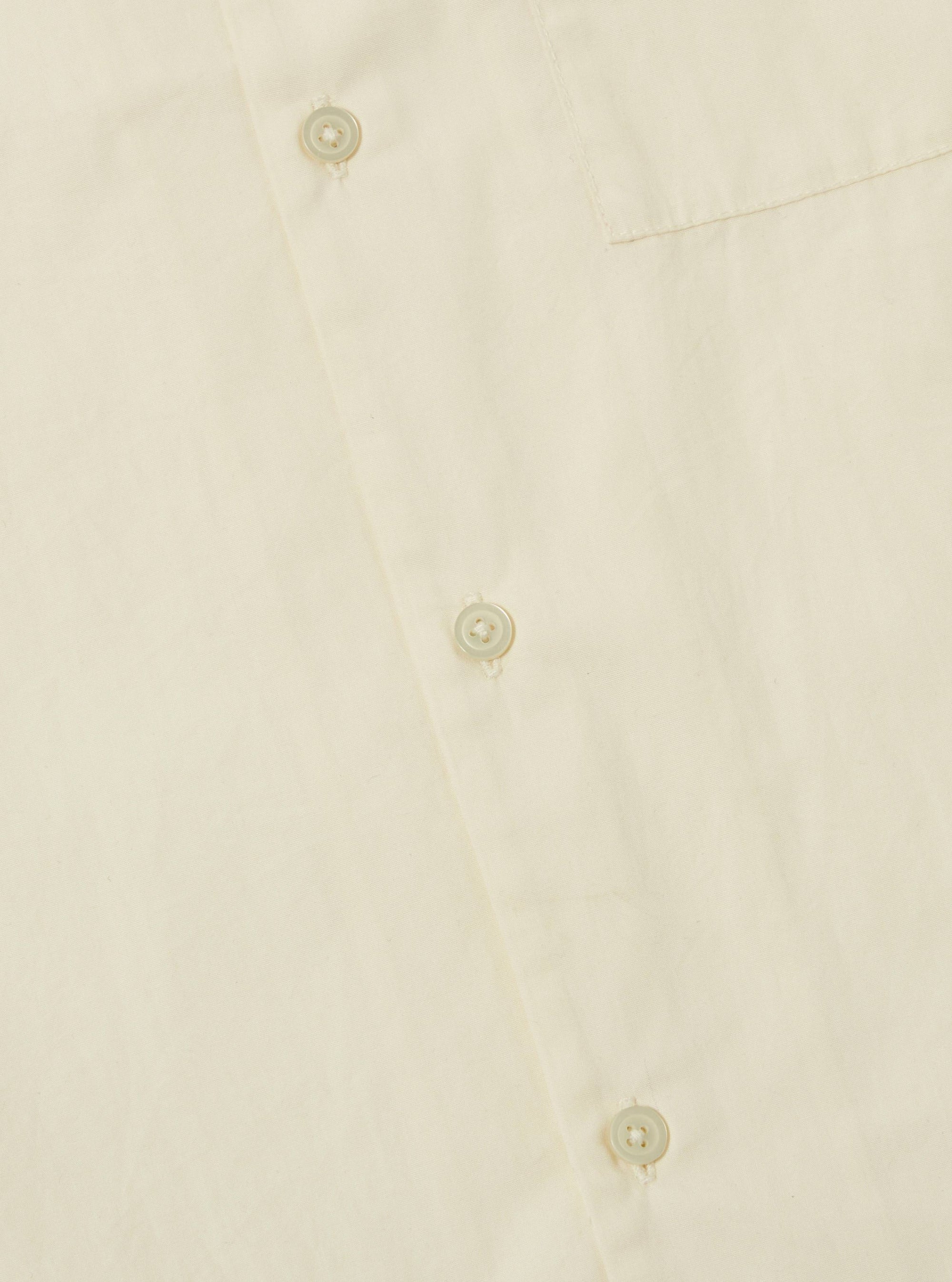 Close-up of the A. SOCIETY x Universal Works Ecru Broadcloth Camp Shirt. Shows the ecru color, broadcloth material, and button details. Shot on a flat surface.