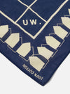 Close-up of the A. SOCIETY x Universal Works Navy Cambric Neckerchief. The navy blue cotton neckerchief has a cream-colored geometric pattern and the letters "UW." on a white background.