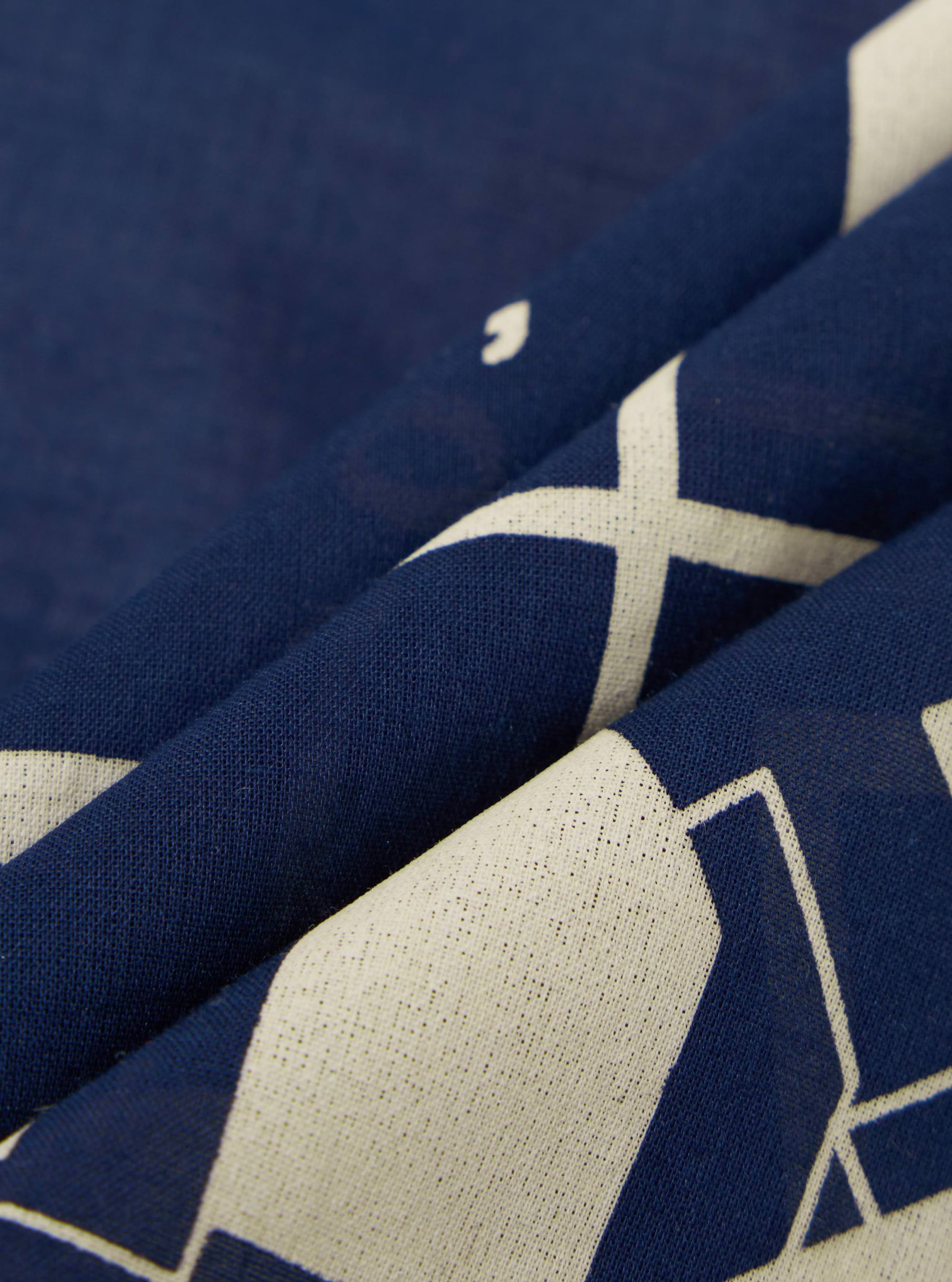 Close-up of the A. SOCIETY x Universal Works Navy Cambric Neckerchief. The navy fabric features a white geometric print and is softly folded on a neutral surface.