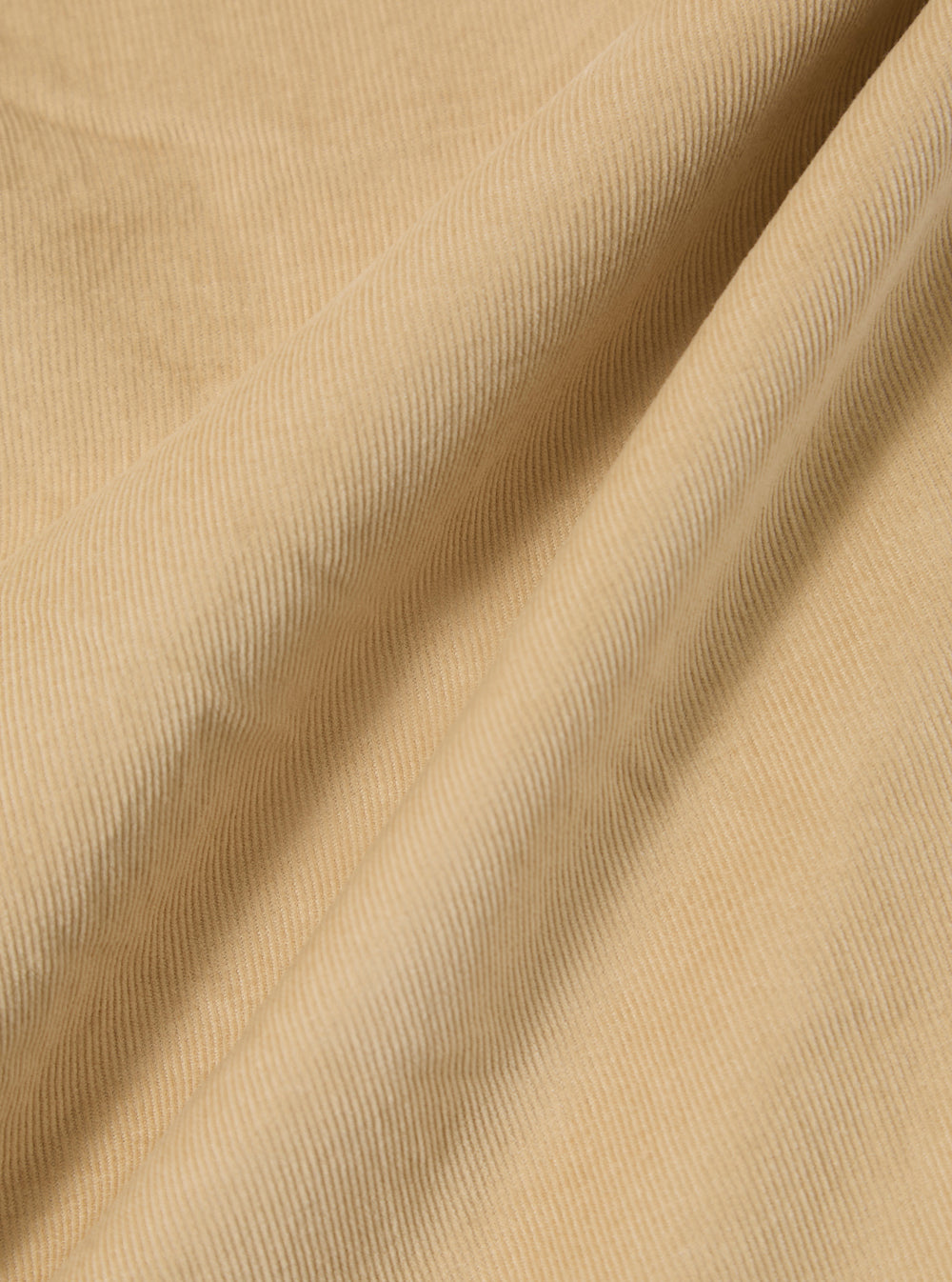 A close-up swatch of the Sand Organic Fine Cord Oxford Pant highlights the fine, vertical 21 wale texture of the organic cotton corduroy. The fabric is a solid, light sand color.