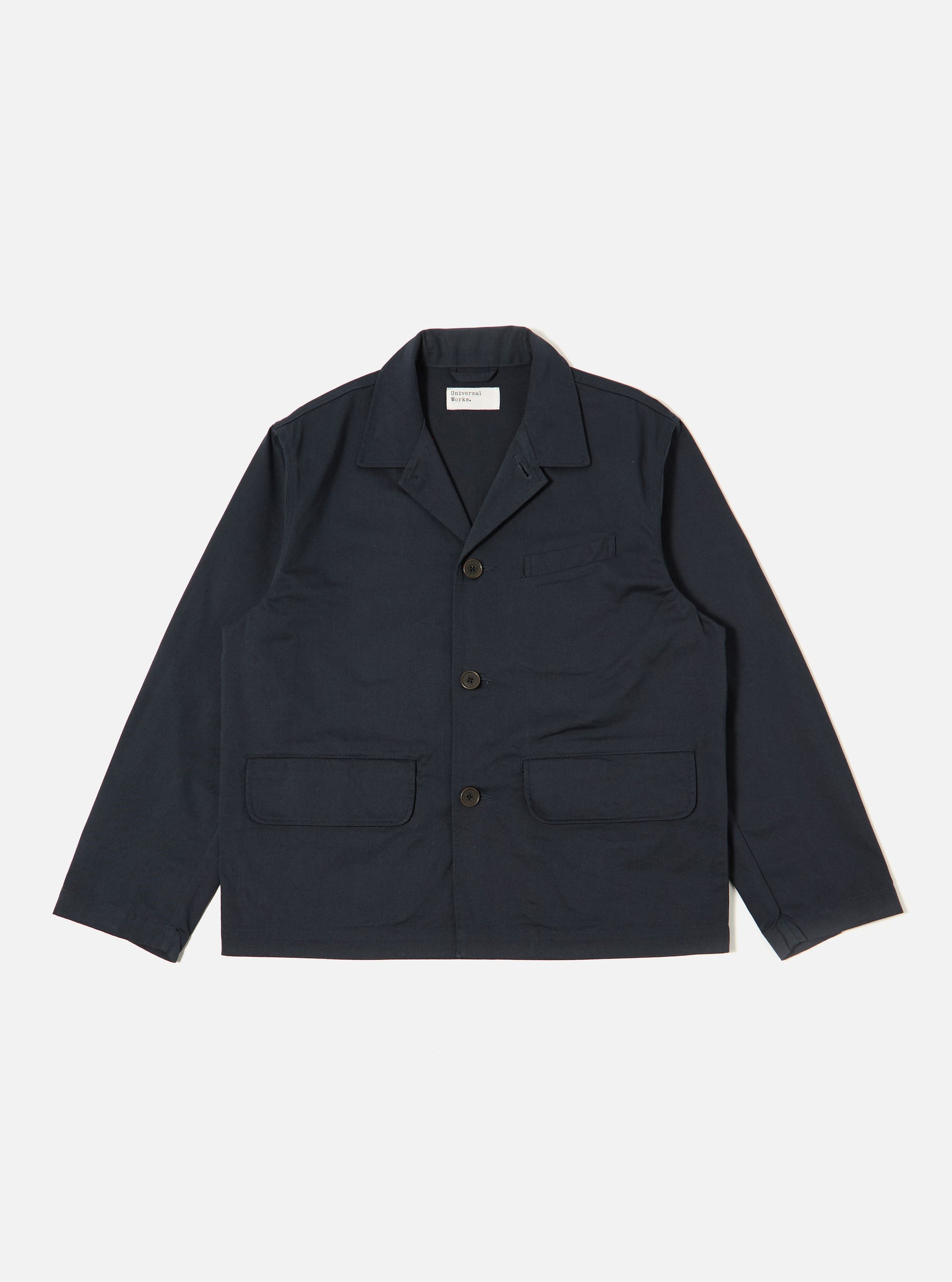 The Navy Twill Franck Jacket is displayed as a flat lay against a plain white background. The jacket features a one-piece flat collar, a central button-front closure, one welt chest pocket, and two large flap pockets at the hips. The garment is made from a structured navy blue cotton twill.
