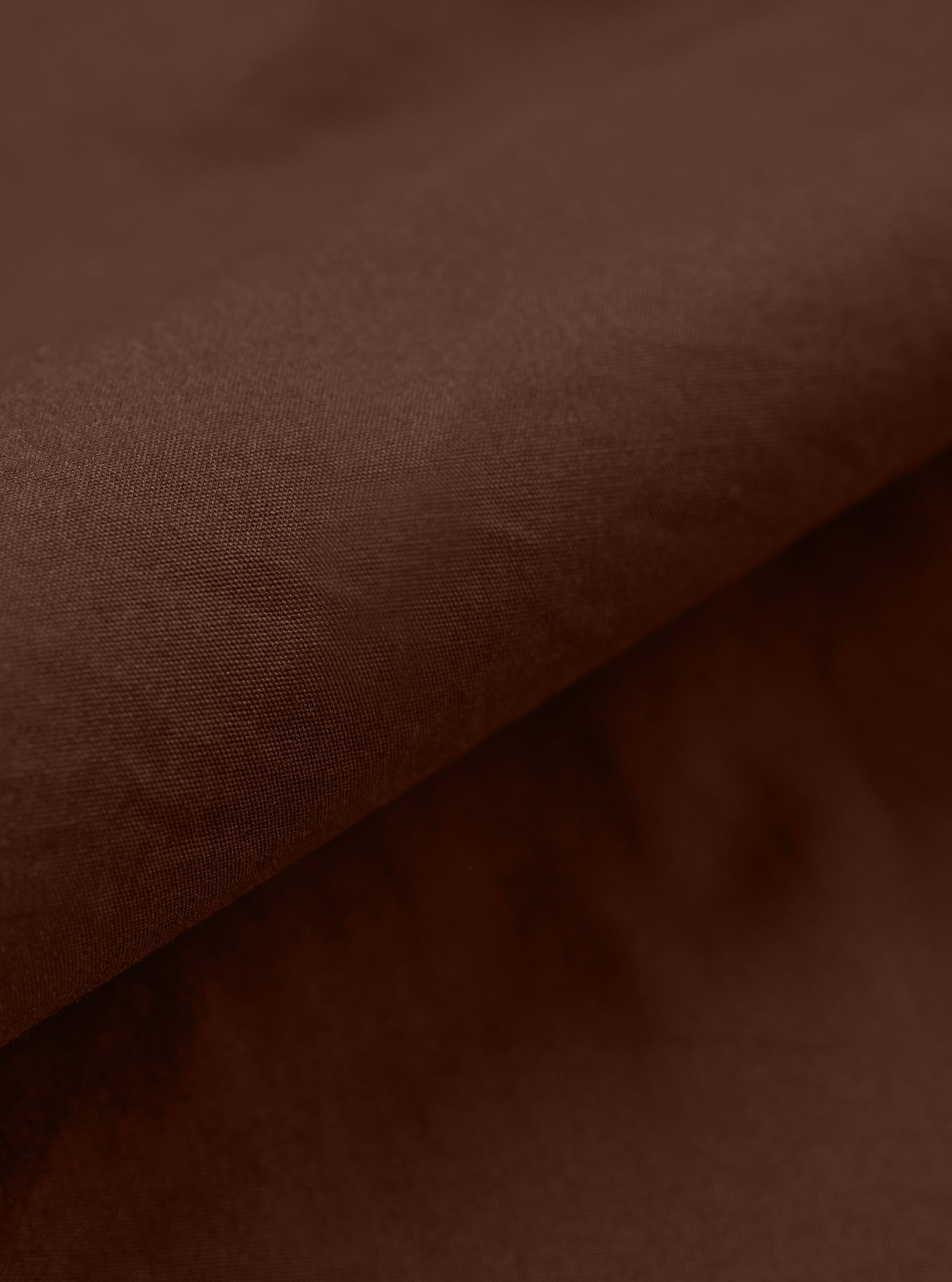A close-up fabric swatch of the Brown Peached Poplin Franck Jacket highlights the rich brown color and the smooth, soft texture of the peached poplin cotton material. The fabric fills the frame, providing a detailed view of the garment's color and finish.