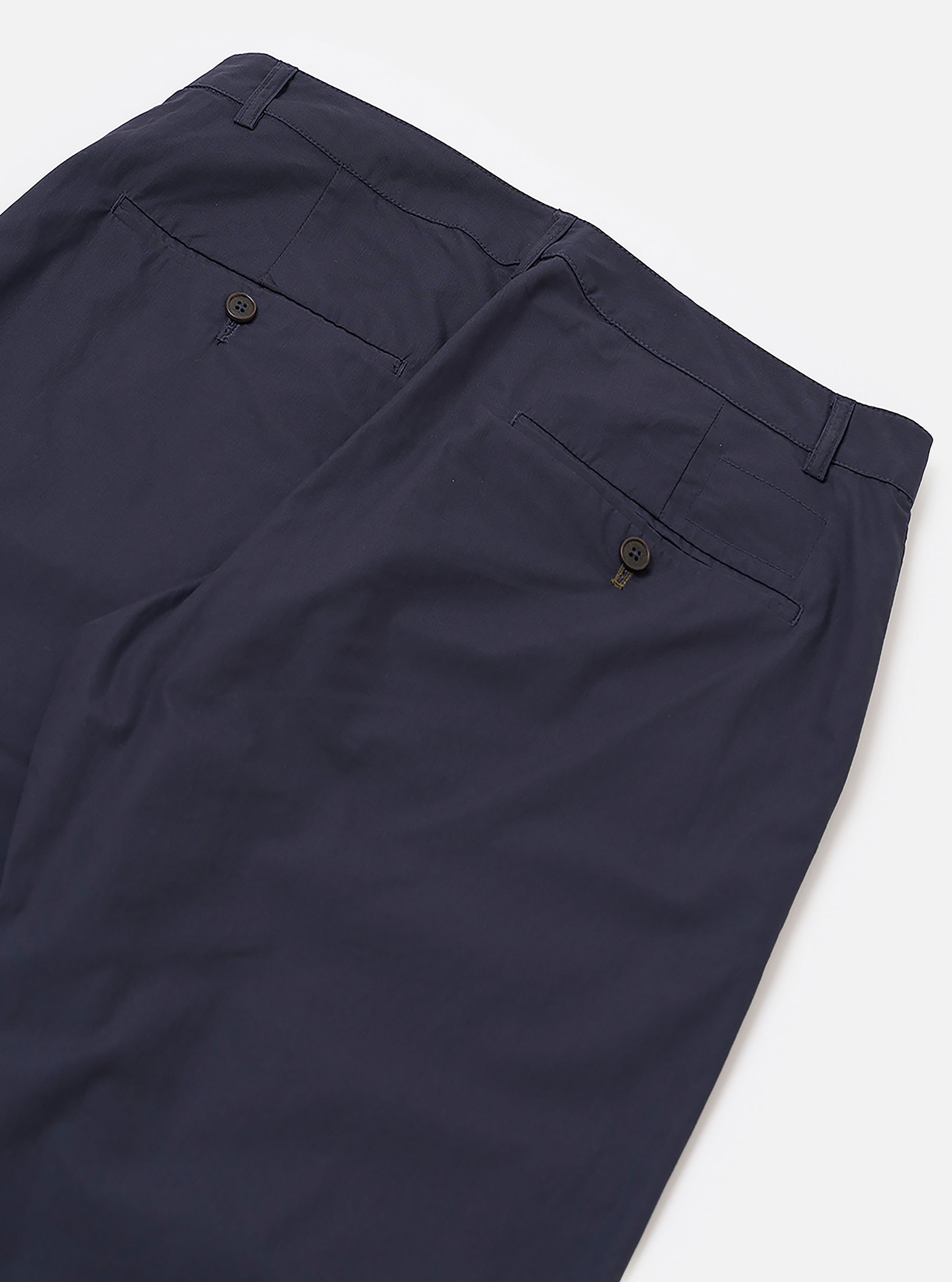 The Navy Peached Poplin Military Chino is shown in a detail view as a flat lay against a plain white background. The image highlights the two rear jetted pockets with button closures and the clean stitching of the back rise. The navy blue cotton fabric has a soft, matte peached finish.