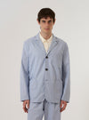 A model wears the Navy Kennedy Stripe Three Button Jacket over a light-colored shirt, standing against a plain white background. The jacket features a three-button front closure, three large patch pockets, and a classic lapel. The fabric has a vertical pinstripe pattern throughout.