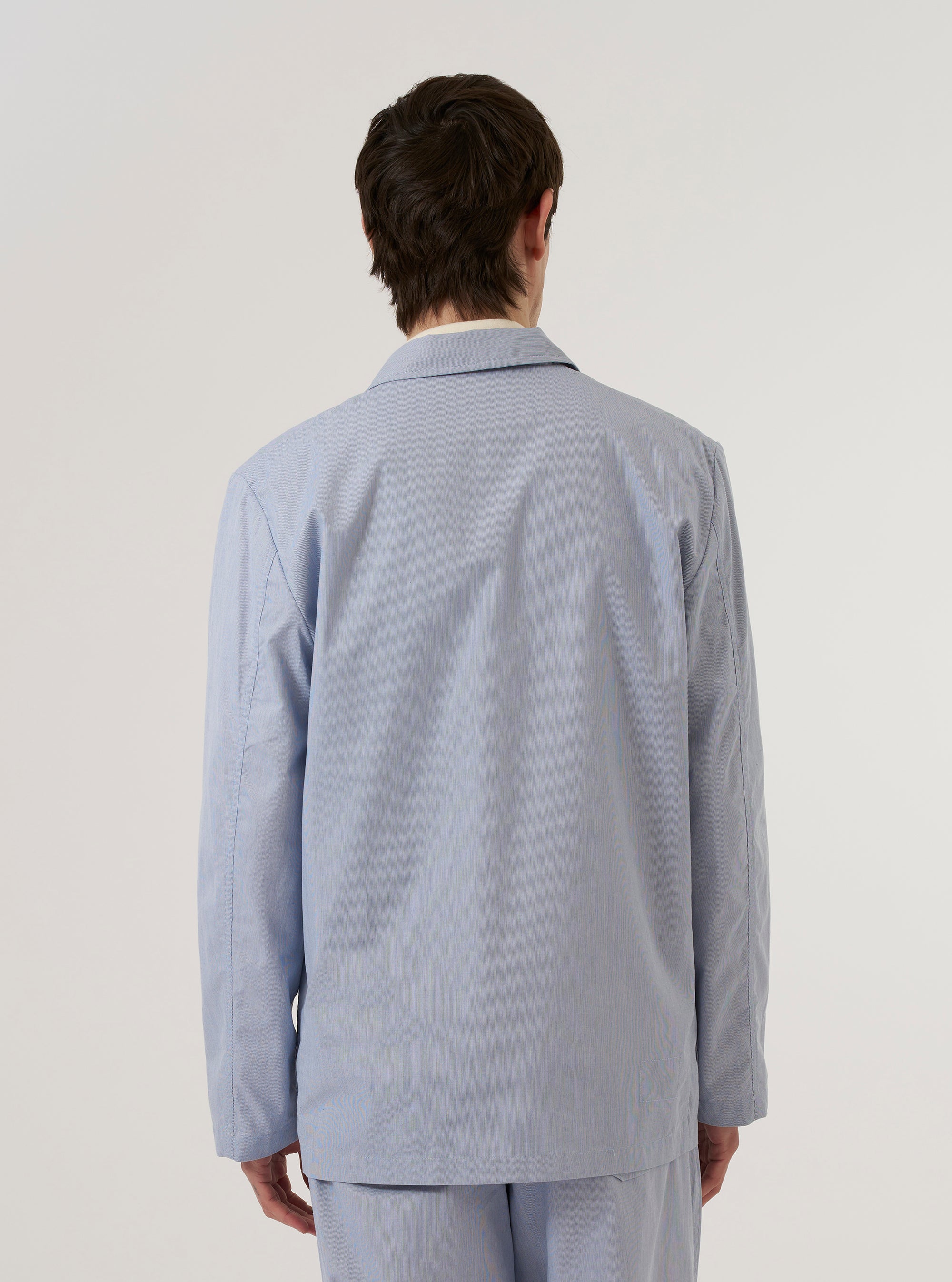 A model wears the Navy Kennedy Stripe Three Button Jacket over a light-colored top against a plain white background. The jacket features a vertical pinstripe pattern, three buttons, and front patch pockets. The image shows the model from the waist up, focusing on the fit and drape of the garment.