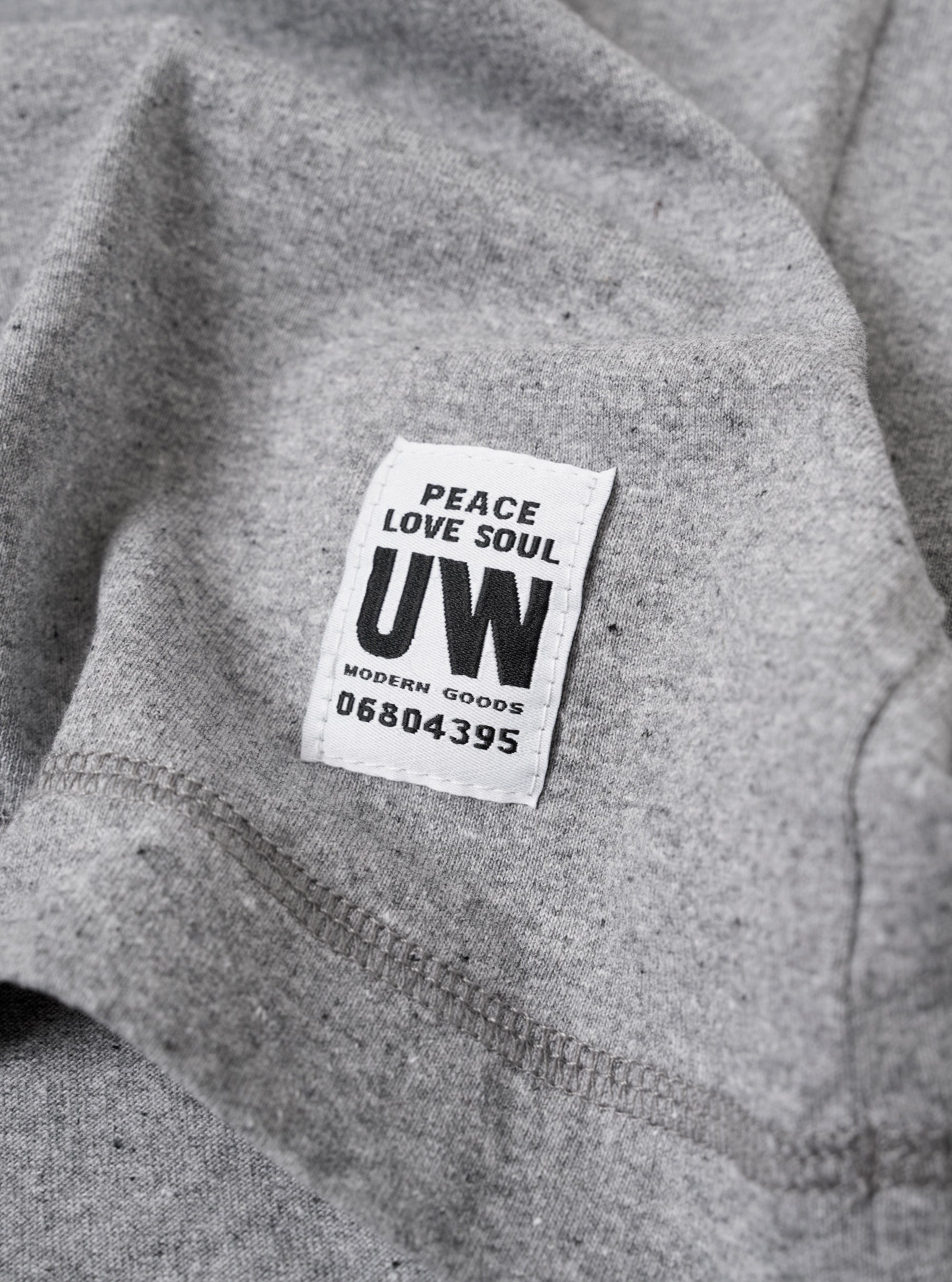 The Grey Marl Recycled/Bio Jersey Henry L/S Tee is shown from a rear angle as a flat lay against a plain white background. The image highlights the simple, clean construction of the long-sleeve t-shirt, featuring a straight hem and a ribbed crew neckline. The fabric is a light grey marl with a soft, jersey texture.
