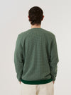 A model wears the Green Argyll Jersey Cardigan over a white t-shirt, shown from a rear three-quarter angle against a plain white background. The cardigan features a relaxed fit, a straight hem, and an all-over dark green argyll pattern on a lighter green base. The model is standing with their back to the camera.