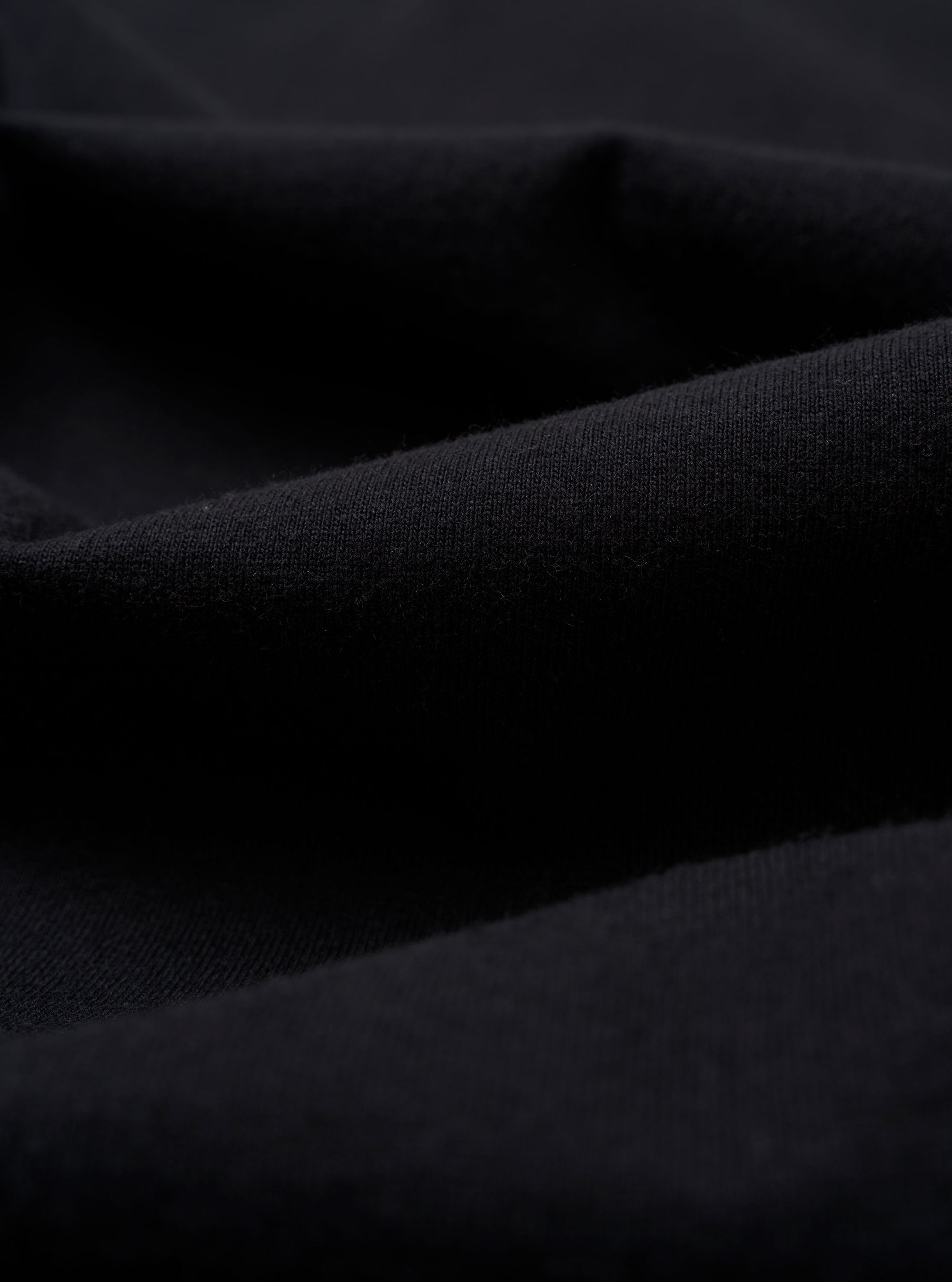 A close-up swatch image of the Black Recycled/Bio Jersey Core Pocket Tee fabric displays a solid black color with a soft, fine jersey knit texture. The fabric fills the entire frame, providing a detailed view of the material.