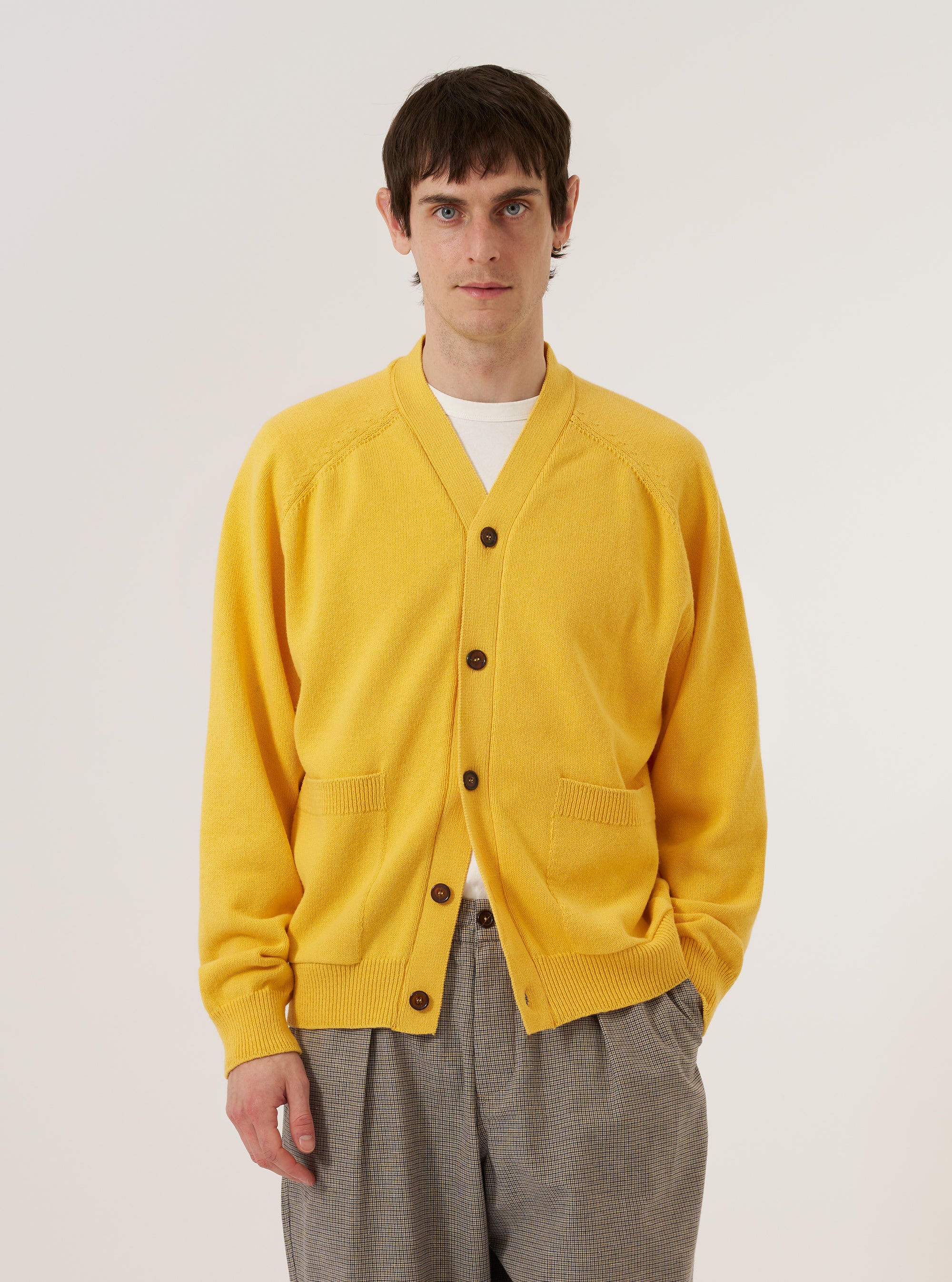 A model wears the Yellow Eco Cotton Knit Pocket David Cardigan against a plain white background. The knit cardigan features a V-neckline, a central button-down closure, and two large patch pockets at the waist. The vibrant yellow garment is shown in a front-facing view, highlighting its textured eco-cotton material.