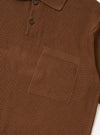 The Brown Fine Texture Tricot S/S Knit Polo is shown in a detail view as a flat lay against a white background. This close-up highlights the polo's rib-knitted fabric, a large square chest pocket, and a two-button placket.