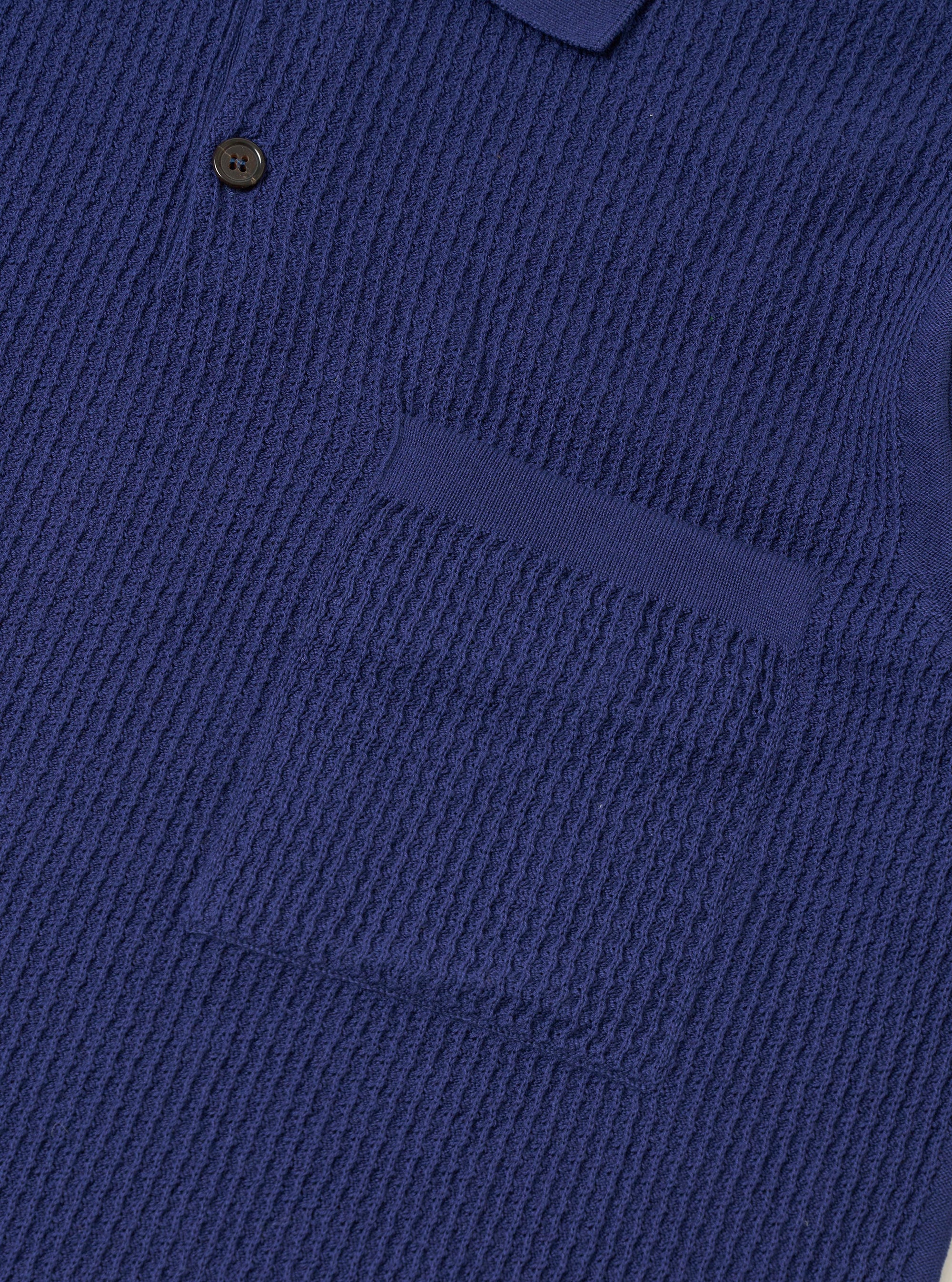 The Navy Fine Texture Tricot S/S Knit Polo is shown from the back as a flat lay against a plain white background. The image highlights the garment's loose, oversized fit and the intricate raised textured rib pattern of the navy cotton fabric. The short sleeves and straight hem are clearly visible.