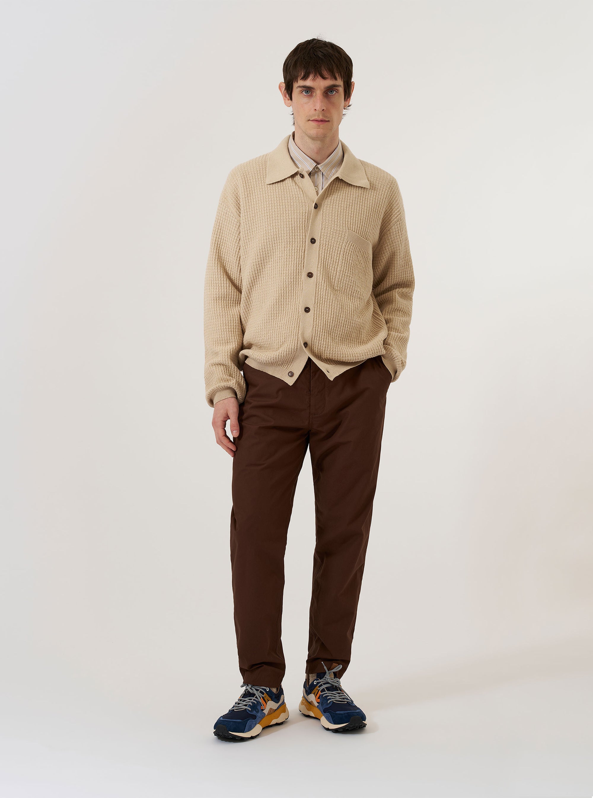 The Sand Eco Cotton Knit Jacket is shown as a flat lay against a plain white background. The jacket features a button-front closure, a fully fashioned collar, and a single large square patch pocket on the chest. The garment has long sleeves with ribbed cuffs and a matching ribbed hem.
