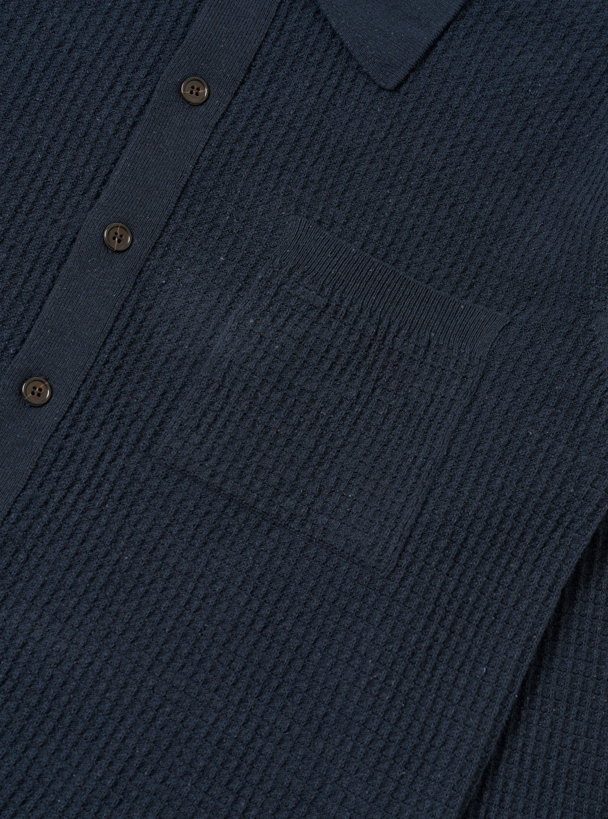 A close-up fabric swatch of the Navy Eco Cotton Knit Jacket highlights the detailed texture of the recycled cotton knit. The deep navy blue yarn is woven into a visible, structured pattern that creates a slightly raised surface.