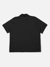 The Black Woolcot Bio S/S Pullover Knit Shirt II is shown from the back as a flat lay against a plain white background. The image highlights the clean, straight-cut back panel, short sleeves, and the smooth, fine-knit texture of the black merino and organic cotton blend fabric.