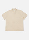 The Ecru Woolcot Bio S/S Pullover Knit Shirt II is shown as a flat lay against a plain white background. This short-sleeved knit shirt features a classic collar, a button placket with two buttons, and a single patch pocket on the left chest. The garment has a boxy fit and is made from a smooth, lightweight ecru-colored knit fabric.
