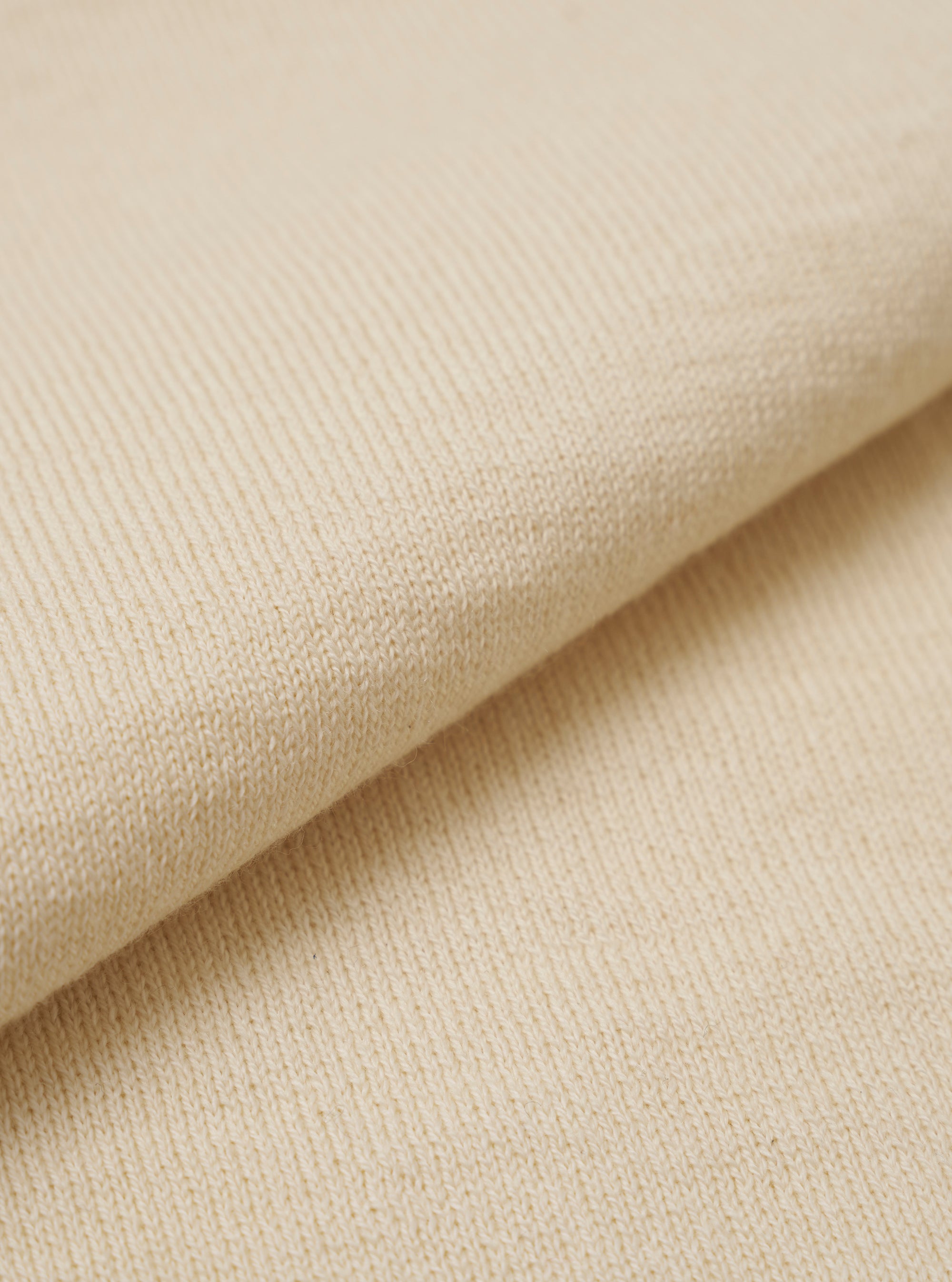 A close-up swatch image of the Ecru Woolcot Bio S/S Pullover Knit Shirt II highlights the fabric's soft, off-white color and smooth, lightweight knit texture. The image focuses on the fine blend of merino wool and organic cotton.