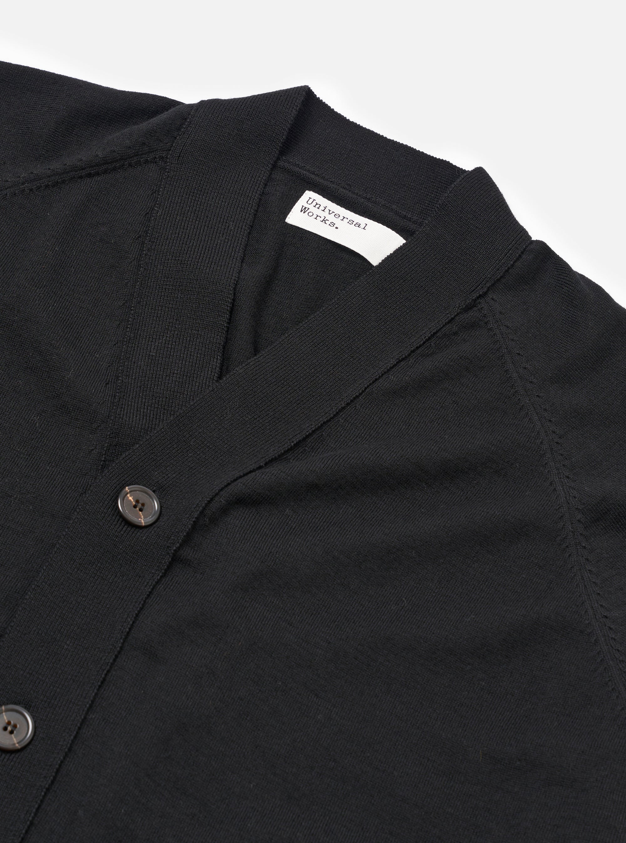 The Black Woolcot Bio Loose Cardigan II is shown from the back as a flat lay against a plain white background. The image highlights the garment's relaxed fit, dropped shoulders, and a simple straight hem. The knit fabric appears soft and uniform in a solid black color.