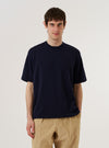 A model wears the Navy Merino Fine Knit Knit Tee against a plain white background. The short-sleeve top features a classic crew neck and a fine-gauge knit texture. The model is shown from the chest up, highlighting the garment's smooth finish and clean-lined fit. No other accessories or layers are visible in the image.