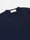 A model wears the Navy Merino Fine Knit Knit Tee against a plain, light-colored background. The image highlights the garment's fine-gauge merino wool texture, featuring a ribbed crew neckline and short sleeves.