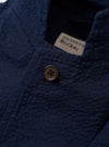 The Navy Derby Stripe Two Button Jacket is shown as a flat lay against a white background. The jacket features a navy and white vertical stripe pattern, two front buttons, a notched lapel, and two large patch pockets at the waist. The hem and sleeves are clearly visible.