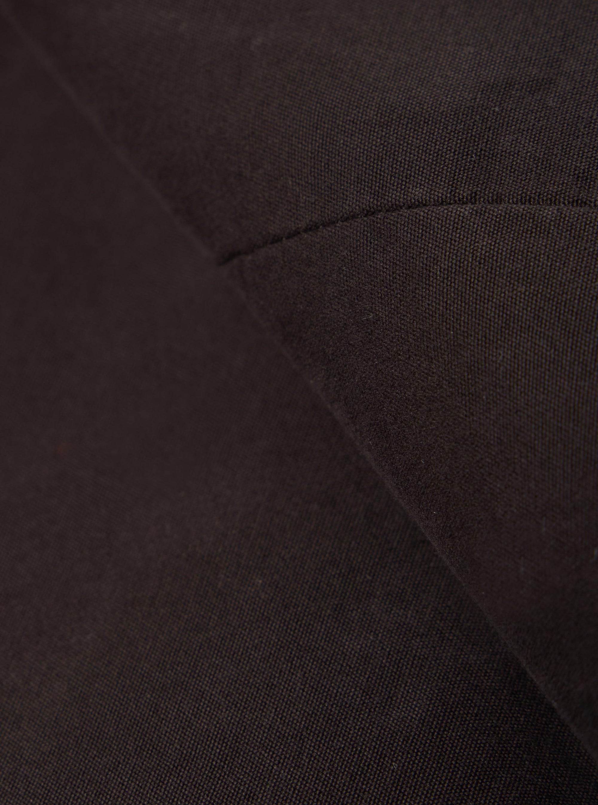 A close-up fabric swatch of the Licorice Summer Canvas Manor Jacket highlights the deep brown color and the dense, textured weave of the summer canvas fabric. The material fills the frame, providing a detailed view of the garment's color and construction.