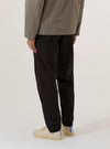 A model wears the Licorice Summer Canvas Military Chino, shown from the waist down against a plain white background. The trousers feature a straight-leg silhouette, side slant pockets, and a clean waistline. The garment is made from a dark licorice brown summer canvas fabric with a visible structured texture.