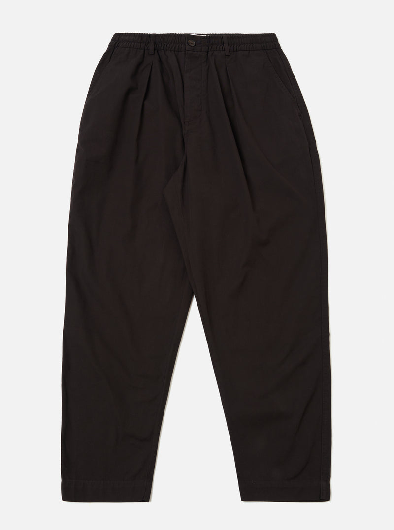 The Licorice Summer Canvas Pleated Track Pant is shown as a flat lay against a plain white background. The trousers feature an elasticated waistband with an internal drawstring, a single pleat on each leg, and a tapered silhouette. The fabric is a solid licorice brown cotton canvas with visible stitching at the hem and pockets.