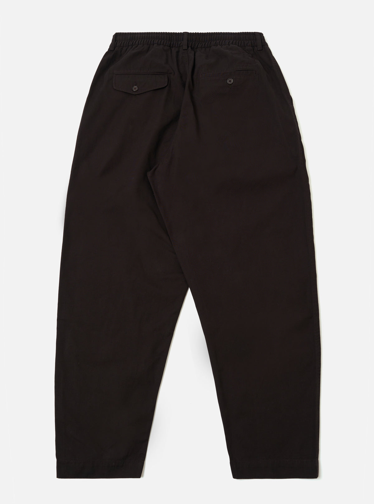 The Licorice Summer Canvas Pleated Track Pant is shown from a rear angle as a flat lay against a plain white background. The image highlights the single rear patch pocket with a buttoned flap and the elasticated waistband. The dark brown cotton canvas fabric features visible stitching details along the seams and hem.