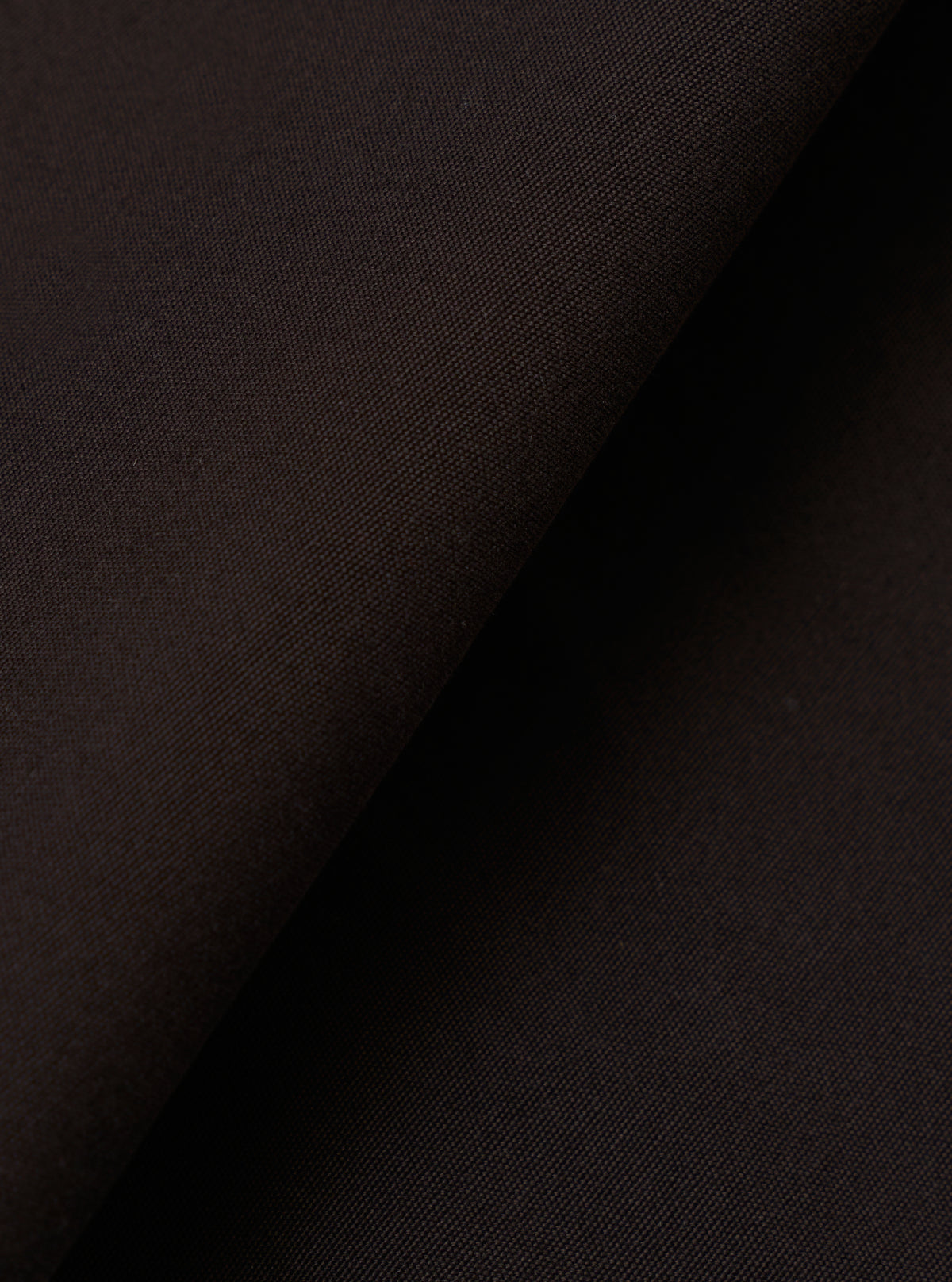 A close-up fabric swatch of the Licorice Summer Canvas Pleated Track Pant highlights the rich licorice brown color and the durable, textured weave of the summer canvas material. The fabric fills the entire frame.
