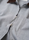 The Light Indigo Jean Cloth Reworked Rose Bowl Jacket is shown from the back as a flat lay against a plain white background. The jacket features a clean, simple construction with a straight hem, a pointed collar, and a locker loop at the nape. The light indigo organic cotton fabric displays a smooth texture and tonal stitching.