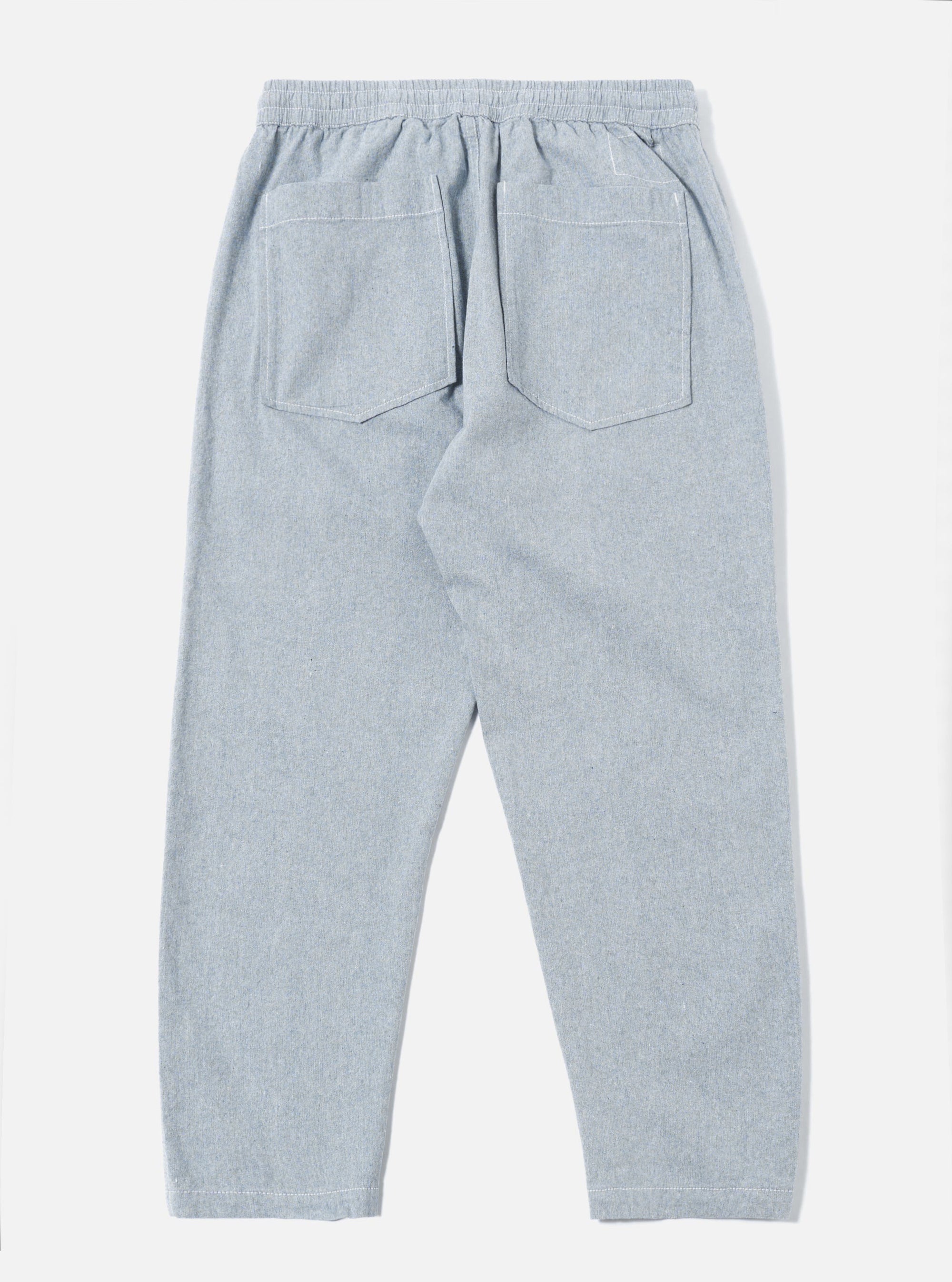 The Light Indigo Jean Cloth Reworked Hi Water Trouser is shown from the back as a flat lay against a plain white background. The image highlights the two rear patch pockets and the elasticated waistband of the light blue organic cotton trousers. The cropped, slim-fit design is visible with clean stitching details along the seams and hem.