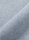 A close-up fabric swatch of the Light Indigo Jean Cloth Reworked Hi Water Trouser displays a light blue indigo denim with a subtle textured weave. The organic cotton fabric is shown in detail, filling the frame to highlight the material's color and construction.