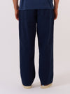 A model wears the Navy Derby Stripe Oxford Pant, shown from a rear three-quarter angle against a plain, neutral studio background. The trousers feature a loose, wide-leg fit and a navy and white vertical stripe pattern. The image highlights the clean back construction and the drape of the striped cotton fabric.