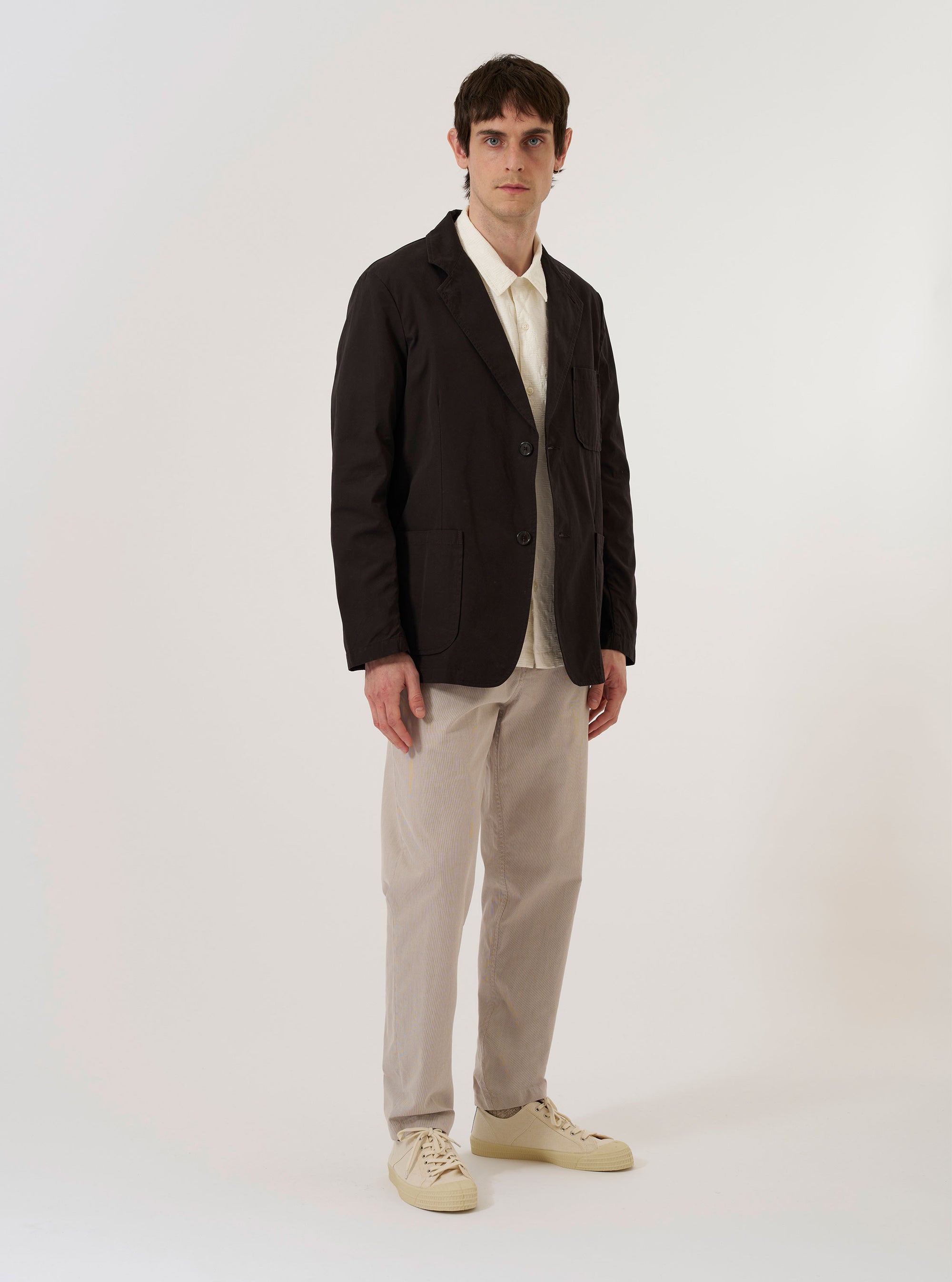 The Licorice Summer Canvas Two Button Jacket is shown as a flat lay against a plain white background. The jacket features a two-button front closure, notched lapels, two large patch pockets at the waist, and a single patch pocket on the left chest. The brown cotton fabric has a visible canvas texture.