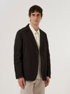 A model wears the Licorice Summer Canvas Two Button Jacket over a dark top, standing against a plain white background. The brown jacket features a loose fit with a two-button front closure, wide notched lapels, and large patch pockets at the waist. The summer canvas fabric has a visible matte texture and a structured appearance.