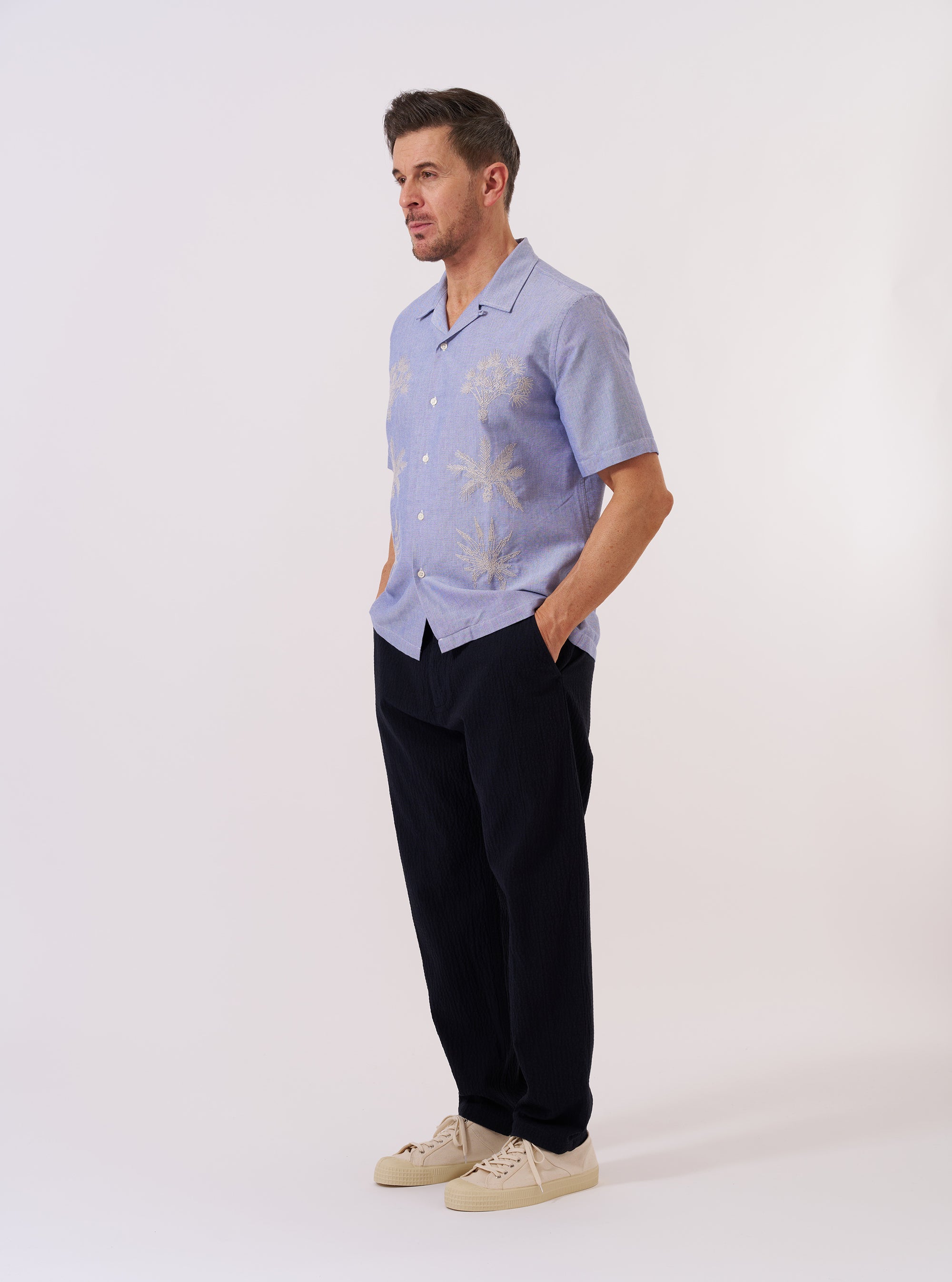 The Blue Oxford Shirting Road Trip Shirt is shown as a flat lay against a plain white background. The shirt features a camp collar, a full button-down front with tonal buttons, and a straight hem. The blue Oxford cloth has a visible textured weave.