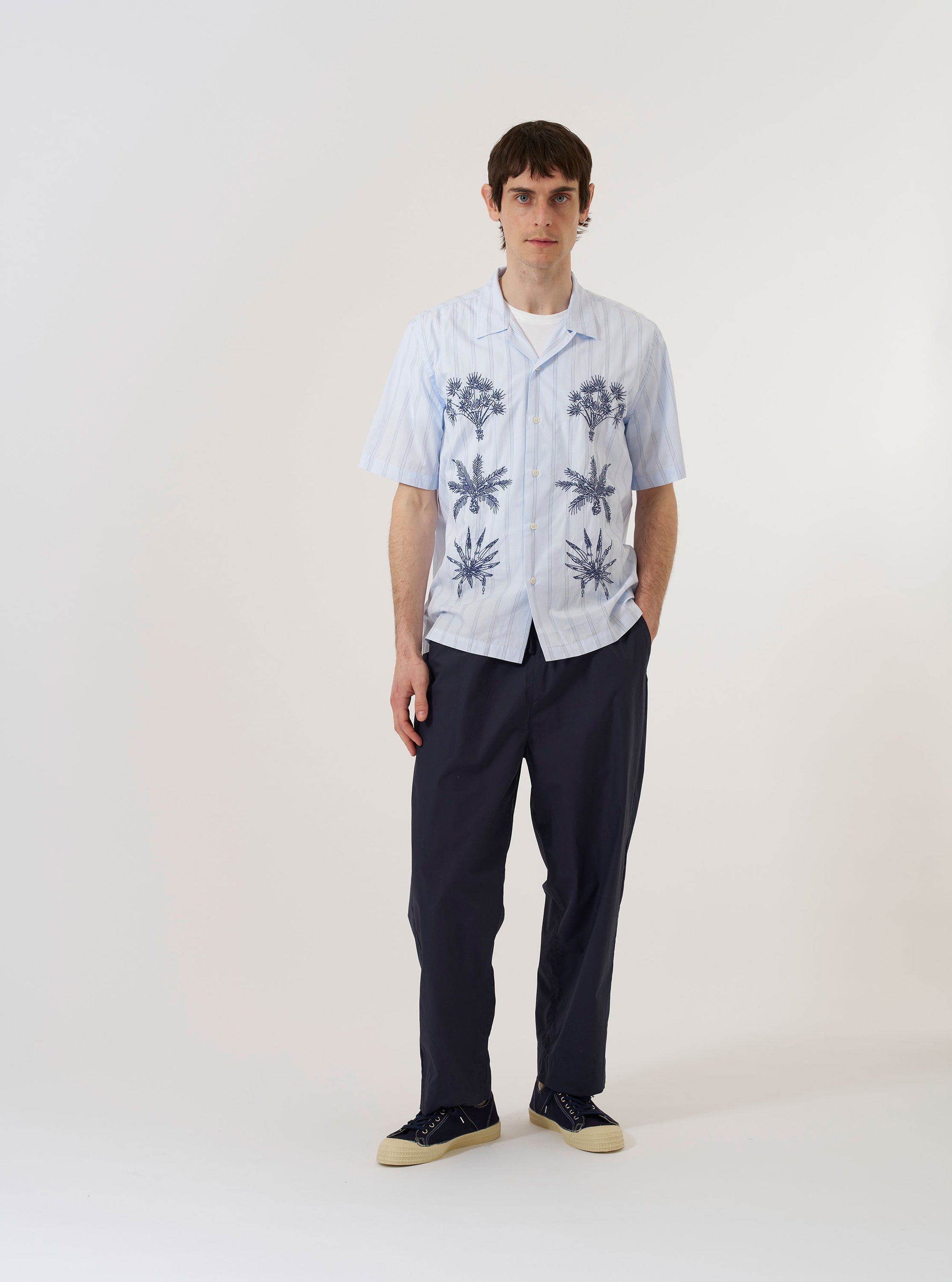 The Soft Blue Mc Stripe Road Trip Shirt is shown as a flat lay against a white background. The shirt features a camp collar, a full-length button-down front, and a straight hem. The fabric is a soft blue with a horizontal stripe pattern.