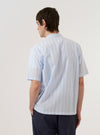 A model wears the Soft Blue Mc Stripe Road Trip Shirt against a plain white background. The shirt features a vertical stripe pattern in soft blue and white, a camp collar, and a single chest pocket. The image shows the model from the waist up, highlighting the fit and collar detail.