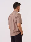 A model is wearing the Brown Sido Linen Mix Road Shirt over a white t-shirt, shown from the back and side as they walk against a plain white background. The image highlights the shirt's relaxed fit, straight hem, and short sleeves. The textured brown linen-blend fabric is clearly visible.