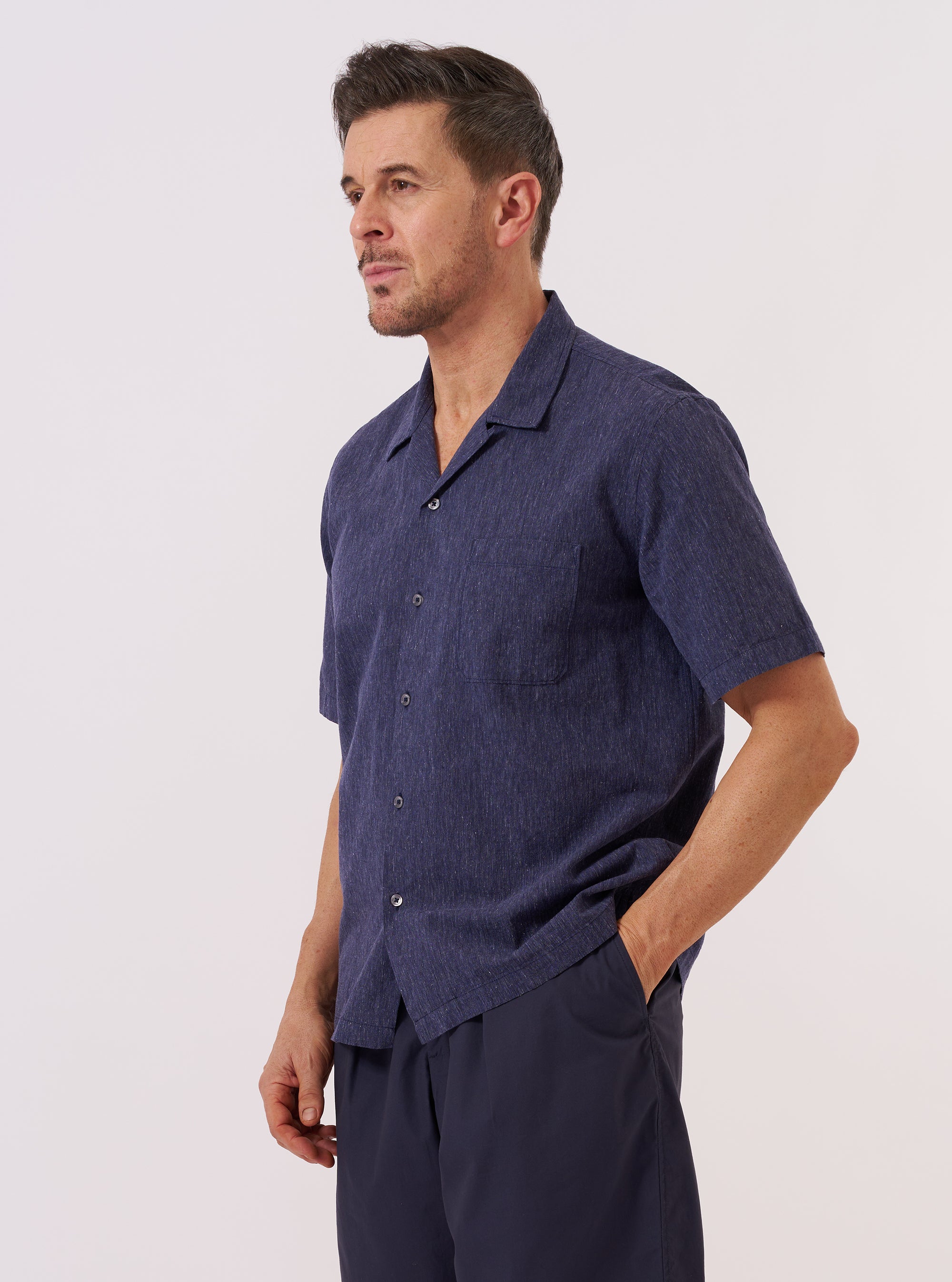 A model wears the Navy Sido Linen Mix Road Shirt over a white t-shirt, standing against a plain white background. The navy blue shirt features a camp collar, a single chest patch pocket, and a full button-down front. The garment is shown from a front-facing view in a studio setting.